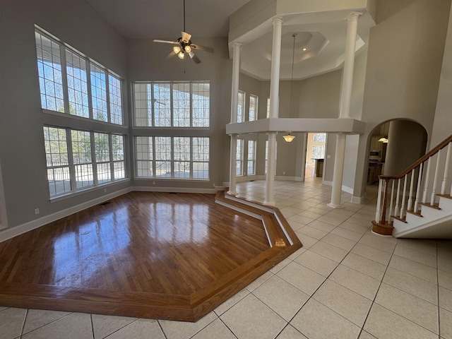 tiled entryway featuring a towering ceiling, baseboards, ornate columns, and ceiling fan