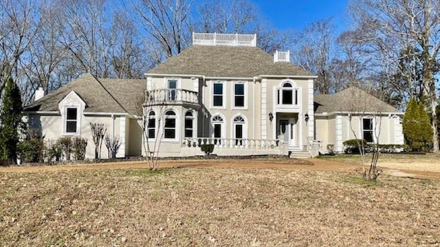 view of front facade featuring a front lawn, a balcony, and a chimney