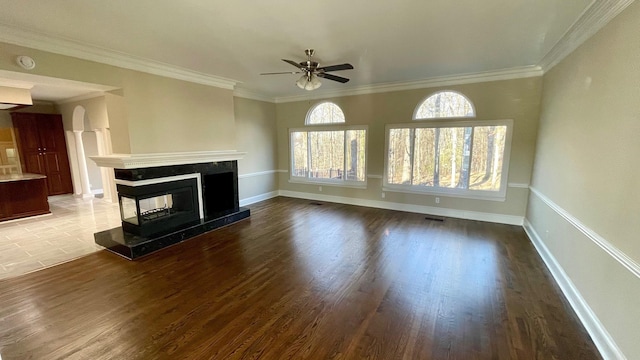 unfurnished living room with crown molding, ceiling fan, baseboards, a tiled fireplace, and wood finished floors