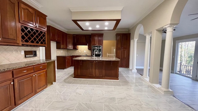 kitchen featuring decorative columns, light stone countertops, arched walkways, and ornamental molding