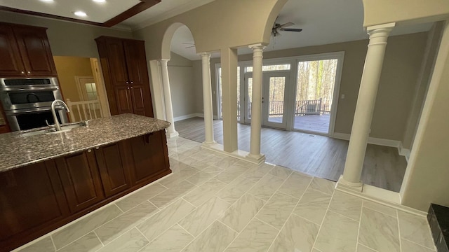 kitchen with arched walkways, ceiling fan, double oven, and ornate columns