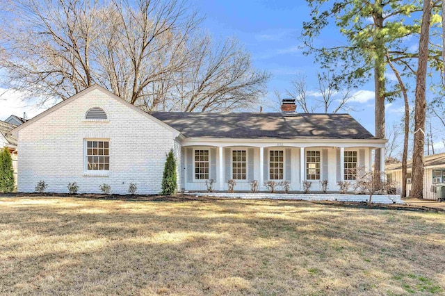 view of front of property featuring a front yard, covered porch, brick siding, and a chimney