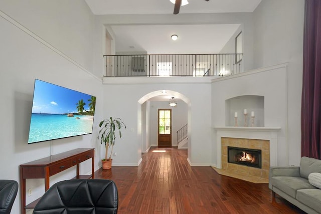 living area featuring wood finished floors, arched walkways, a towering ceiling, and a tile fireplace