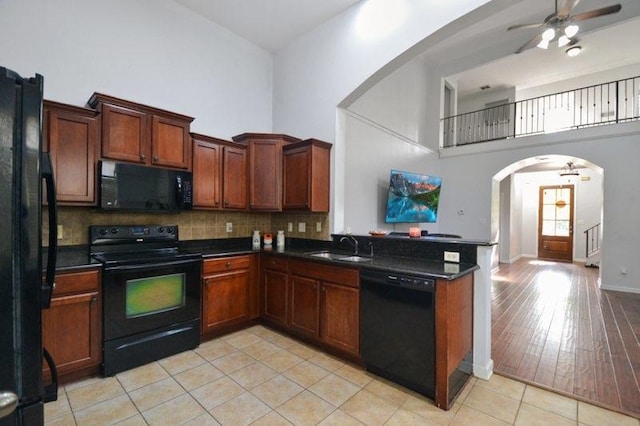 kitchen with a high ceiling, arched walkways, a sink, black appliances, and dark countertops