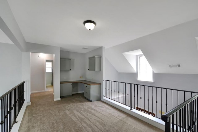 unfurnished office with baseboards, visible vents, built in study area, lofted ceiling, and light carpet