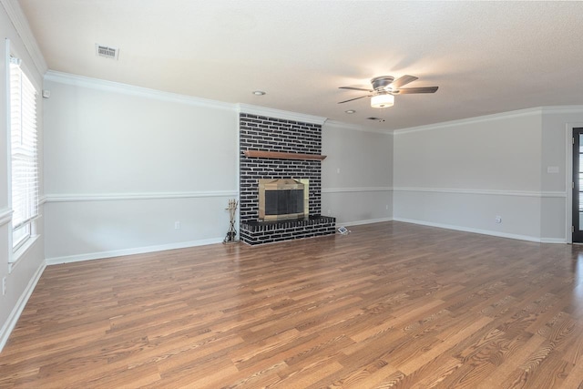 unfurnished living room featuring a ceiling fan, crown molding, a brick fireplace, and wood finished floors