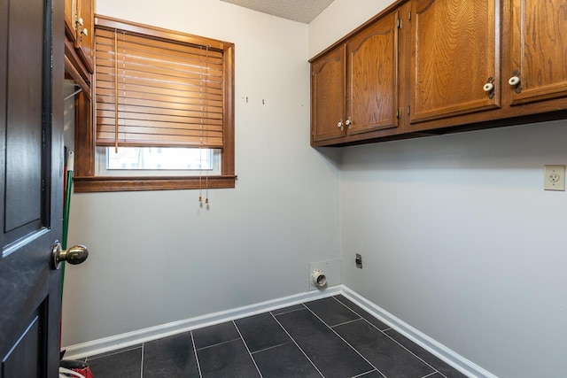 washroom with electric dryer hookup, baseboards, dark tile patterned floors, and cabinet space