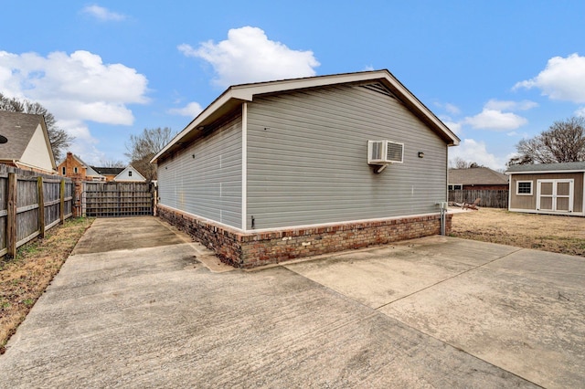 view of property exterior with an AC wall unit, fence private yard, a storage shed, a patio area, and an outbuilding