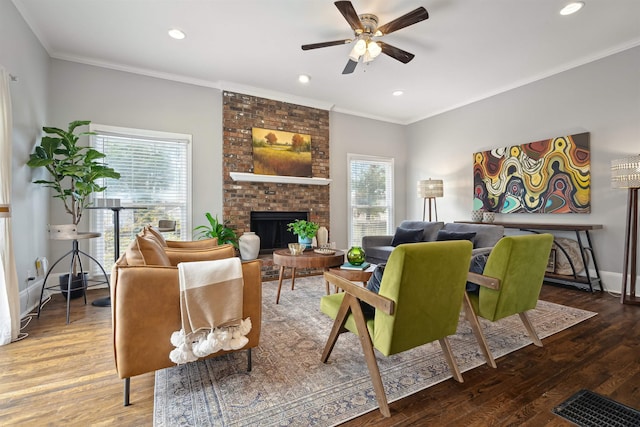 living room featuring a brick fireplace, crown molding, baseboards, and wood finished floors