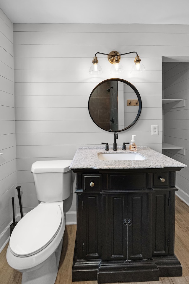 bathroom featuring wooden walls, baseboards, toilet, wood finished floors, and vanity