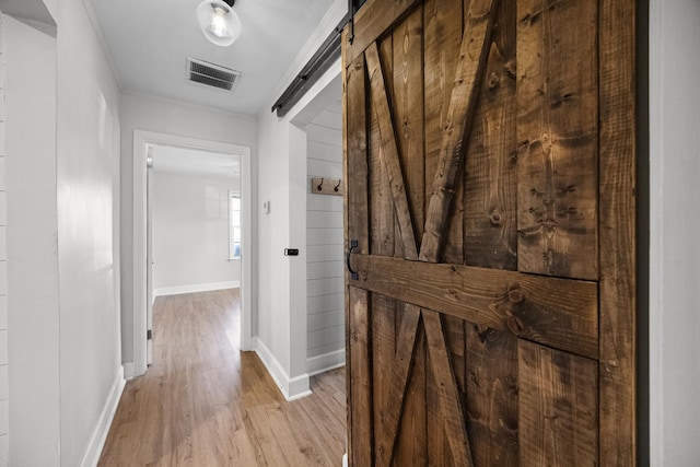 hall featuring a barn door, baseboards, visible vents, and light wood-style flooring