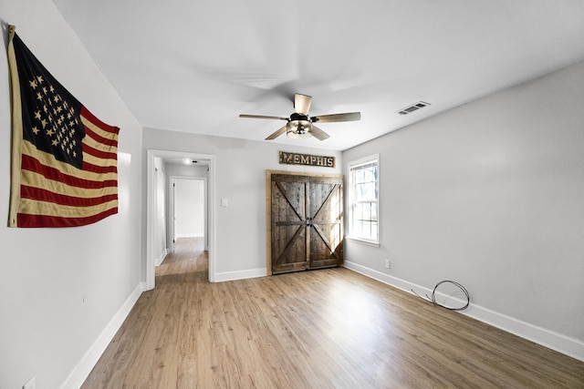 unfurnished room with a ceiling fan, wood finished floors, visible vents, and baseboards