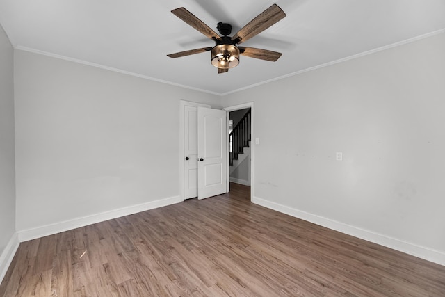 empty room featuring ceiling fan, crown molding, baseboards, and wood finished floors