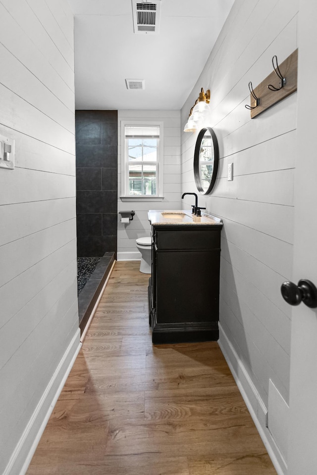 bathroom with visible vents, tiled shower, toilet, and wood finished floors