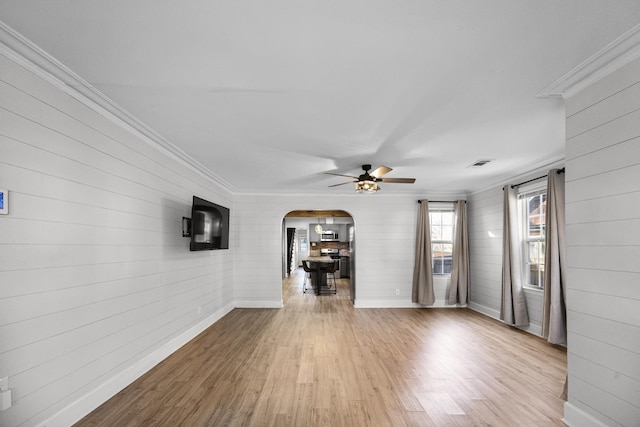 unfurnished living room with visible vents, baseboards, ornamental molding, wood finished floors, and arched walkways