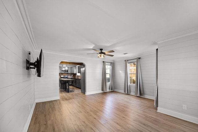 unfurnished living room with crown molding, light wood-style flooring, and arched walkways