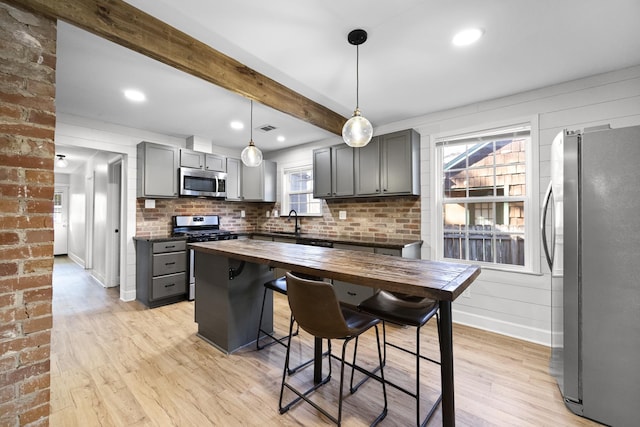 kitchen with light wood finished floors, gray cabinetry, appliances with stainless steel finishes, wood counters, and beamed ceiling