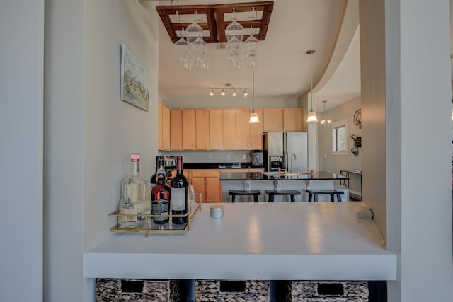 kitchen featuring dark countertops, light brown cabinets, decorative light fixtures, a kitchen bar, and stainless steel refrigerator with ice dispenser