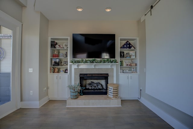 unfurnished living room with a tiled fireplace, built in shelves, baseboards, and wood finished floors