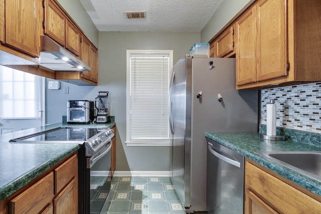 kitchen with brown cabinetry, tasteful backsplash, under cabinet range hood, and stainless steel appliances