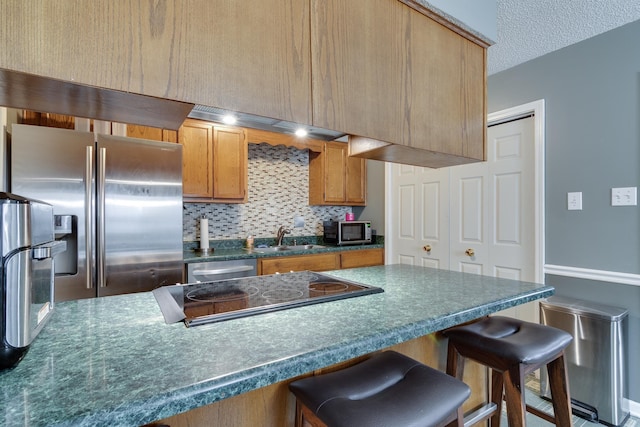 kitchen featuring a breakfast bar, a sink, appliances with stainless steel finishes, dark countertops, and tasteful backsplash