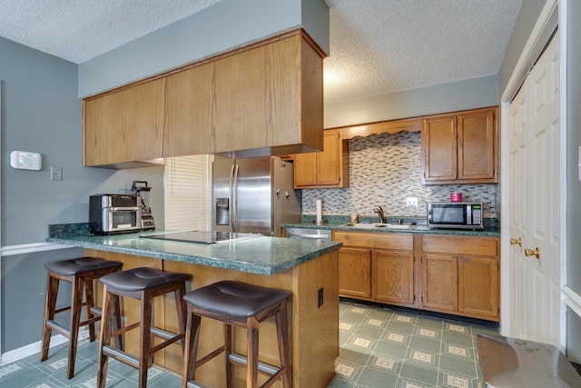 kitchen featuring a sink, a kitchen breakfast bar, dark countertops, stainless steel appliances, and a peninsula