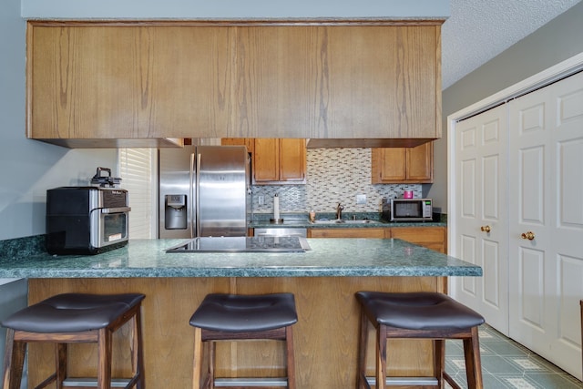 kitchen with brown cabinets, a sink, a kitchen breakfast bar, stainless steel appliances, and a peninsula