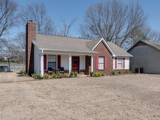 ranch-style house featuring fence, covered porch, a shingled roof, a chimney, and brick siding