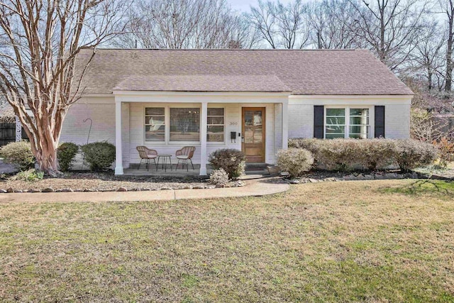 ranch-style house with brick siding, covered porch, a front lawn, and roof with shingles