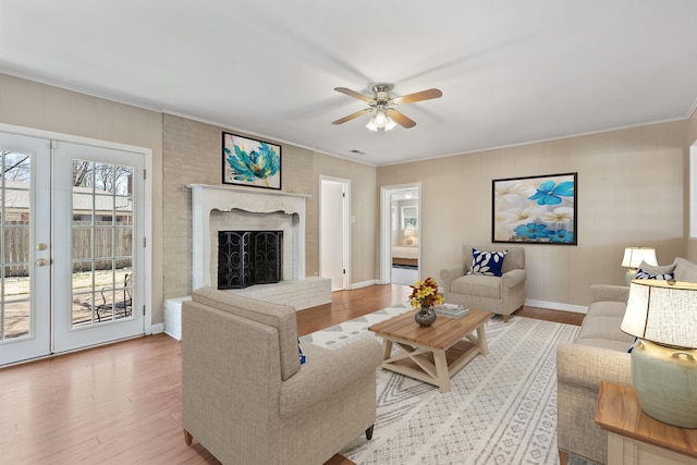 living room featuring a ceiling fan, wood finished floors, baseboards, ornamental molding, and a brick fireplace