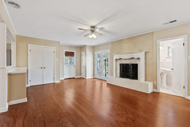 unfurnished living room with visible vents, a brick fireplace, french doors, and wood finished floors