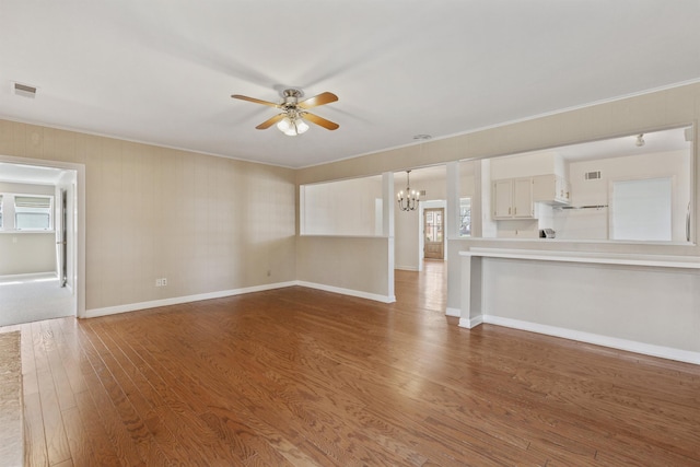 unfurnished living room with visible vents, wood finished floors, crown molding, and ceiling fan with notable chandelier