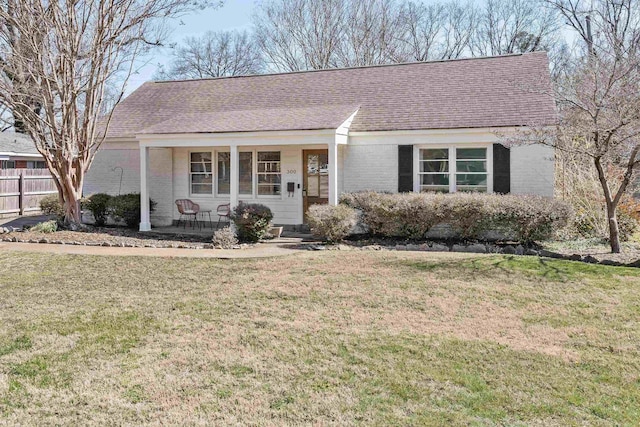 ranch-style home with a front yard, fence, roof with shingles, a porch, and brick siding