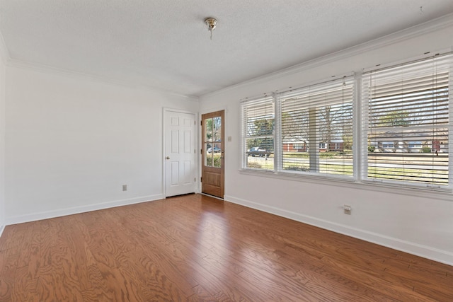 spare room with baseboards, a textured ceiling, wood finished floors, and crown molding