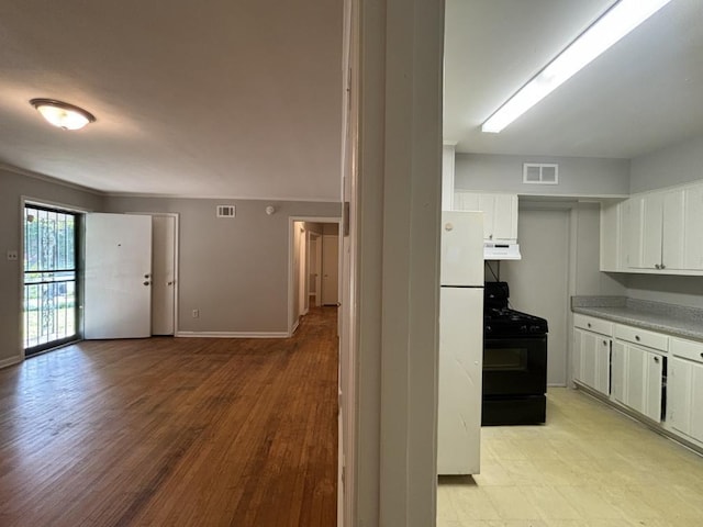 kitchen featuring visible vents, freestanding refrigerator, black range with gas stovetop, under cabinet range hood, and white cabinetry