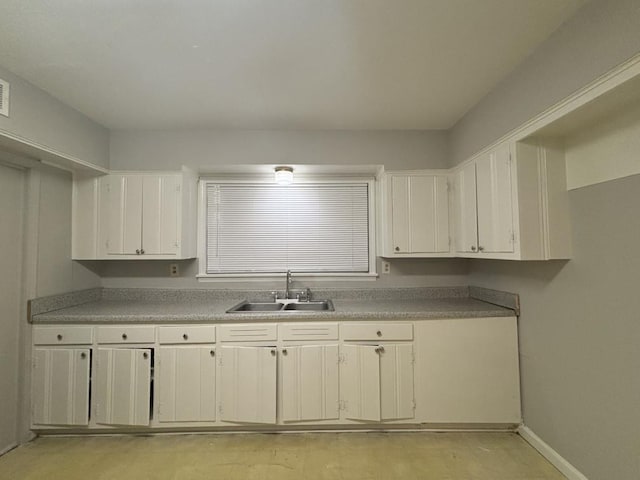 kitchen with a sink, baseboards, light countertops, and white cabinetry