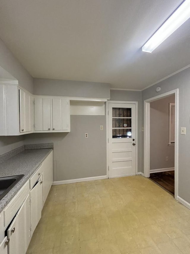 kitchen featuring white cabinets, light floors, crown molding, and baseboards