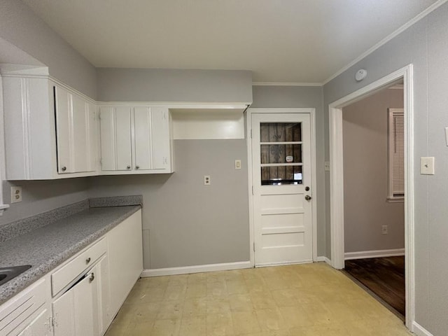 kitchen featuring white cabinets, crown molding, light countertops, baseboards, and light floors