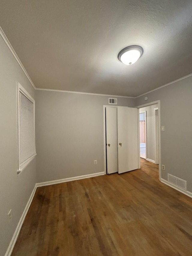 unfurnished bedroom featuring visible vents, crown molding, baseboards, and wood finished floors