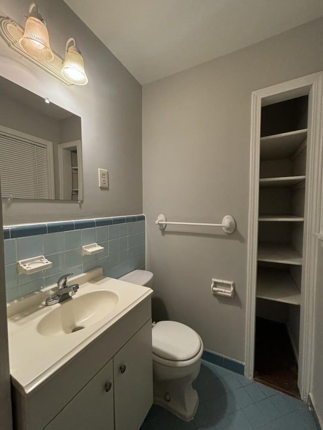 half bathroom with tile patterned flooring, toilet, vanity, and tile walls