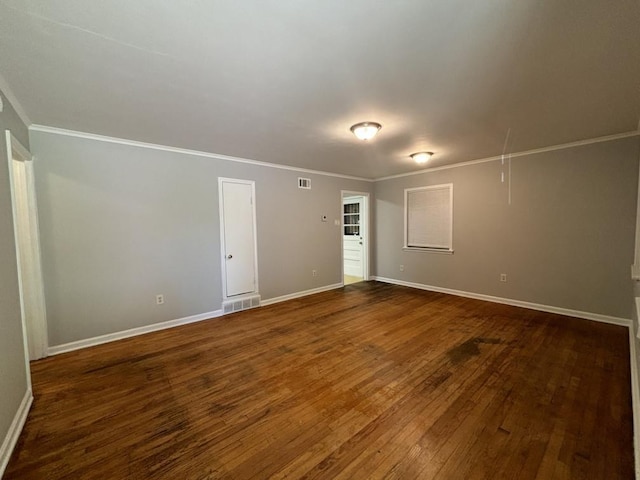 empty room with attic access, dark wood-type flooring, baseboards, and ornamental molding