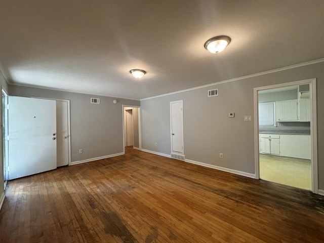 empty room with crown molding, wood finished floors, and visible vents