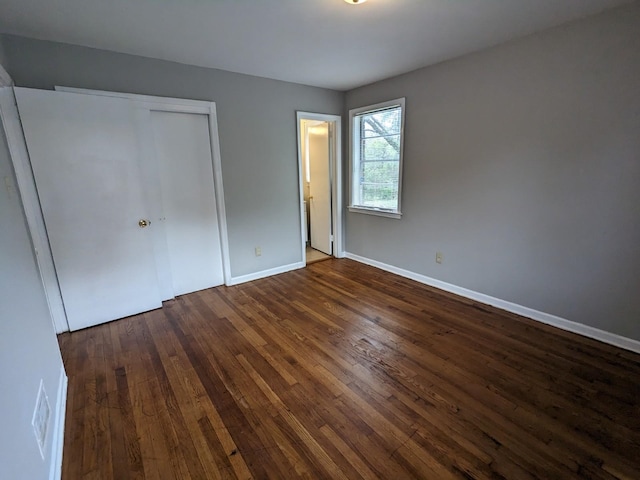 unfurnished bedroom with a closet, baseboards, and dark wood-style floors