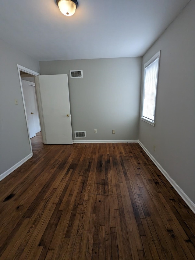 unfurnished room with visible vents, dark wood-type flooring, and baseboards