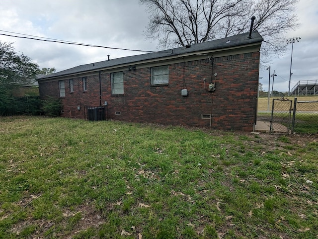 back of property featuring a lawn, fence, crawl space, brick siding, and central AC unit