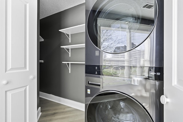 laundry room with a textured ceiling, stacked washer and clothes dryer, laundry area, and a healthy amount of sunlight