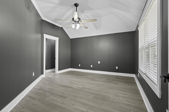 spare room with wood finished floors, a ceiling fan, baseboards, ornamental molding, and vaulted ceiling