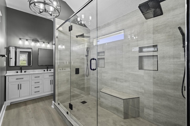 full bathroom with double vanity, a shower stall, wood finished floors, and a sink