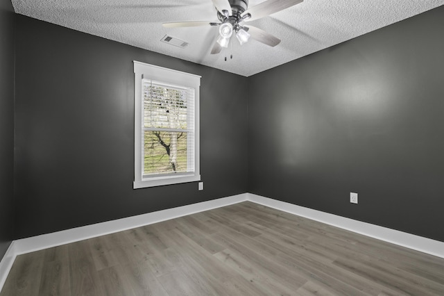 spare room featuring visible vents, a textured ceiling, wood finished floors, baseboards, and ceiling fan