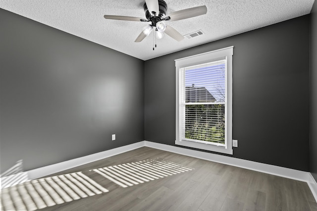 unfurnished room with visible vents, ceiling fan, baseboards, wood finished floors, and a textured ceiling